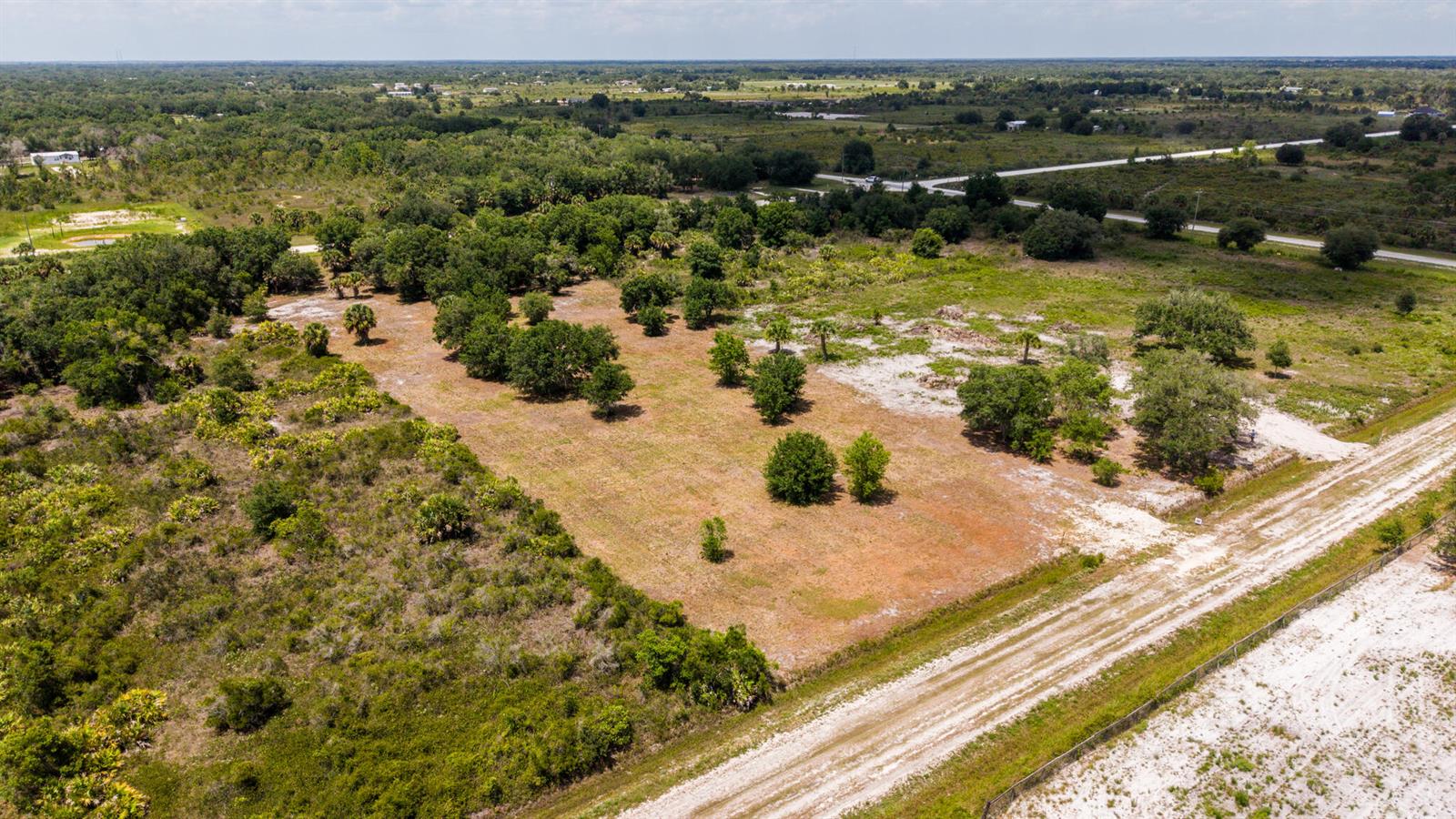 An aerial view shows a cleared, grassy lot with scattered trees and a dirt road — 19371 NW 254th Street, Okeechobee FL 34972, OKEECHOBEE, FL