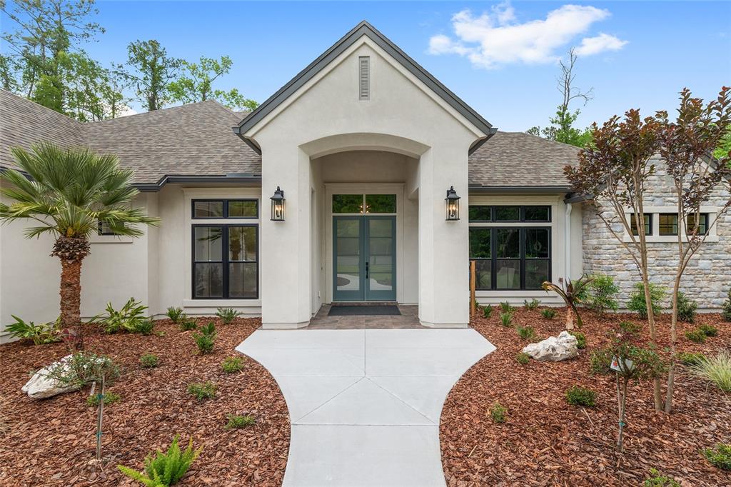 A front view of a single-story house with a stucco facade, stone accents, and double doors — 5990 NW 88TH WAY, GAINESVILLE, FL