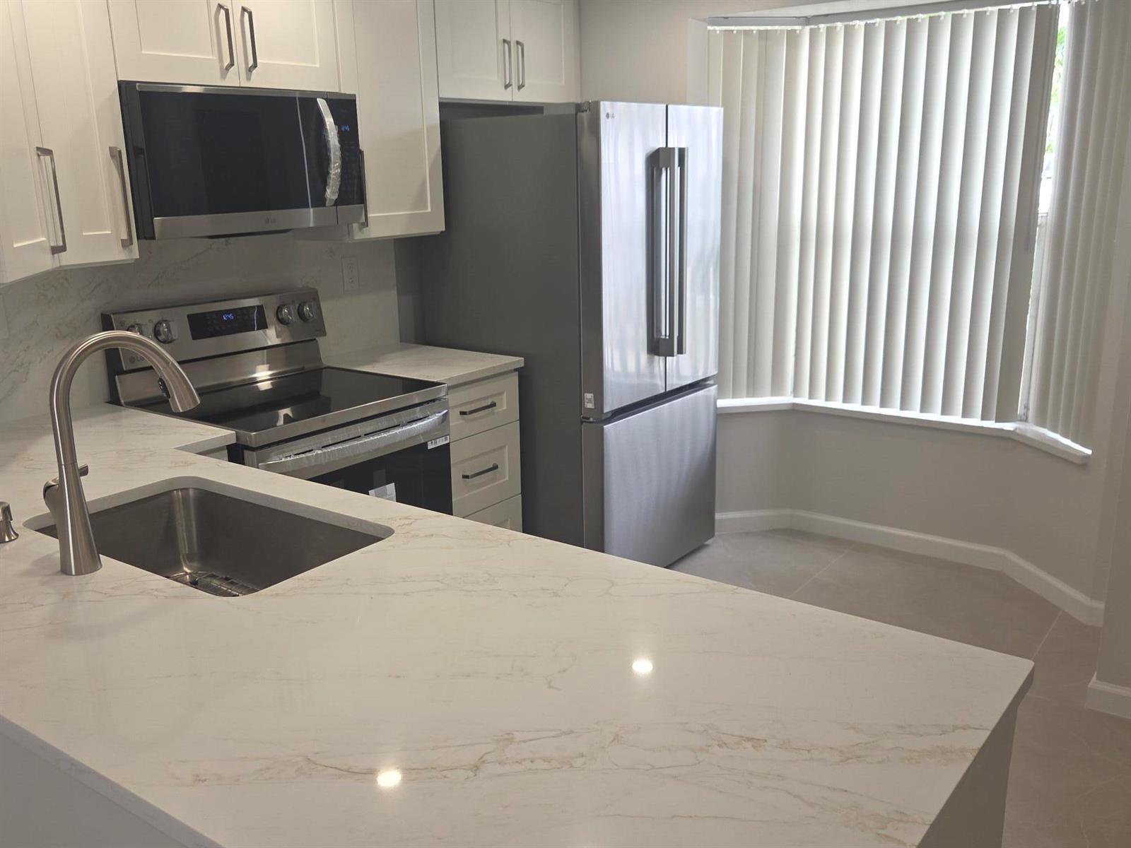 A modern kitchen features white cabinets, stainless steel appliances, and a marble-patterned countertop — 2843 NE 15th Street, Pompano Beach FL 33062, POMPANO BEACH, FL