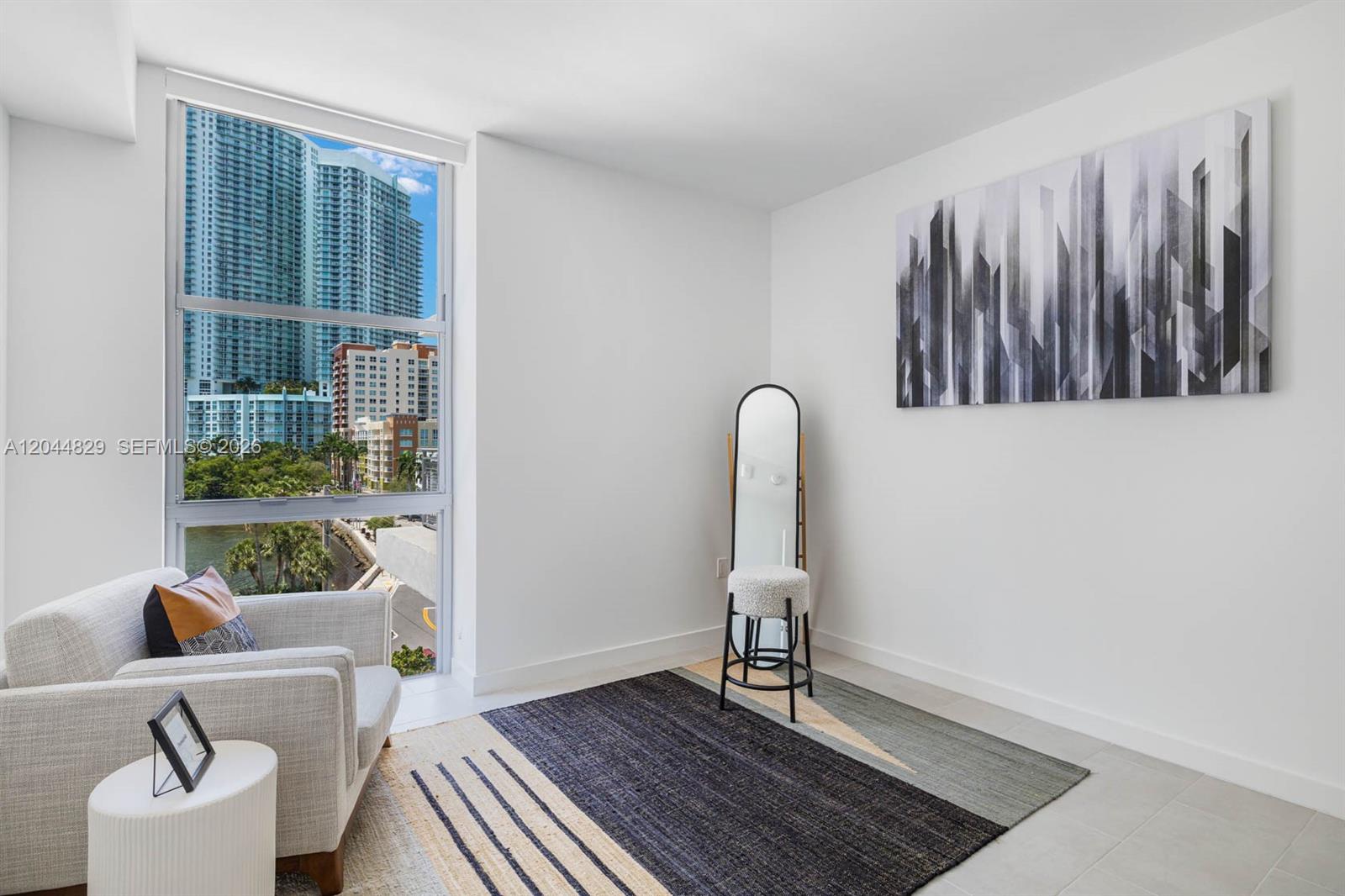 A modern room features a chair, a mirror, a rug, and a large city view window — 2150 N Bayshore Dr # 1602, Miami FL 33137, MIAMI, FL