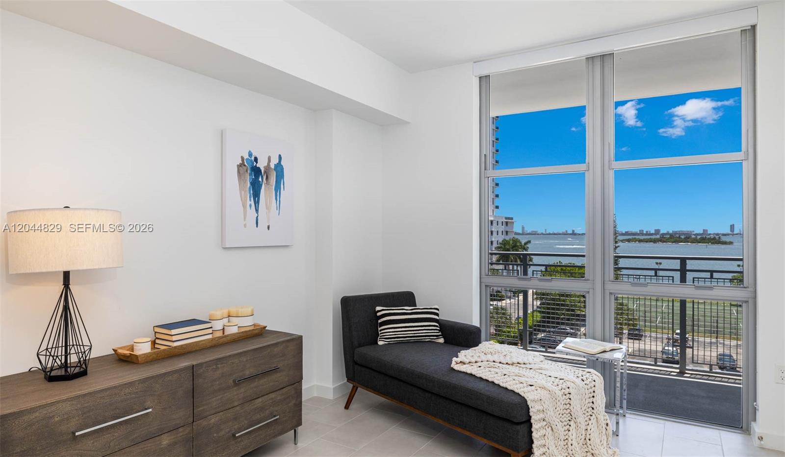 A room features a dark chaise lounge, a wooden dresser, and floor-to-ceiling windows with water views — 2150 N Bayshore Dr # 1602, Miami FL 33137, MIAMI, FL