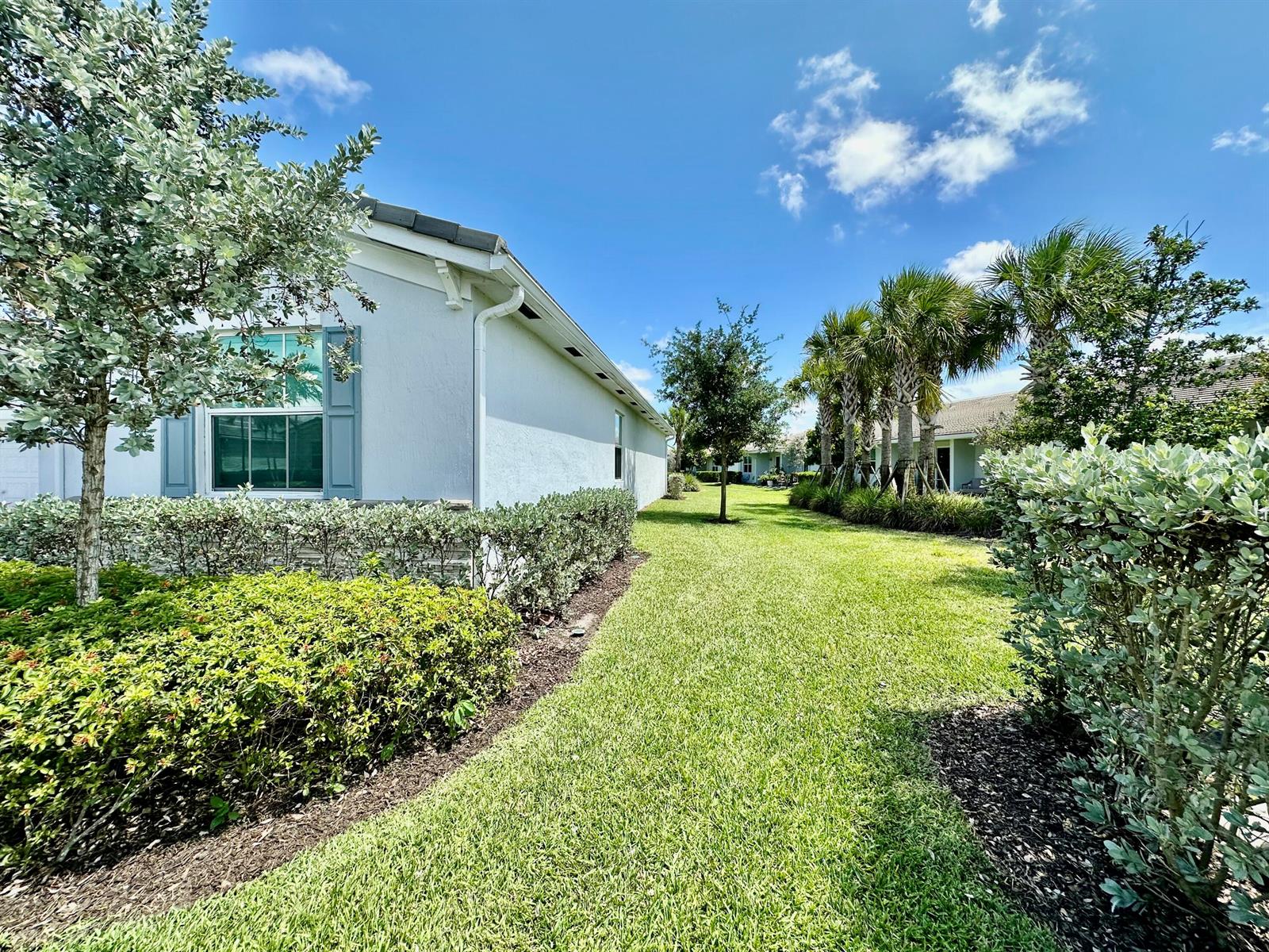 A side view of a light-colored house with blue shutters, landscaping, and a grassy yard — 7036 Peters Lane, Delray Beach FL 33446, DELRAY BEACH, FL