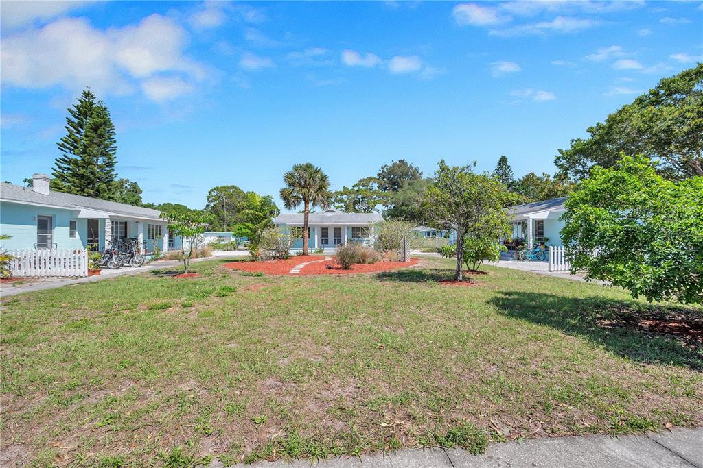 A grassy courtyard sits between two light blue cottages under a bright blue sky — 5027 28TH AVENUE S, GULFPORT, FL