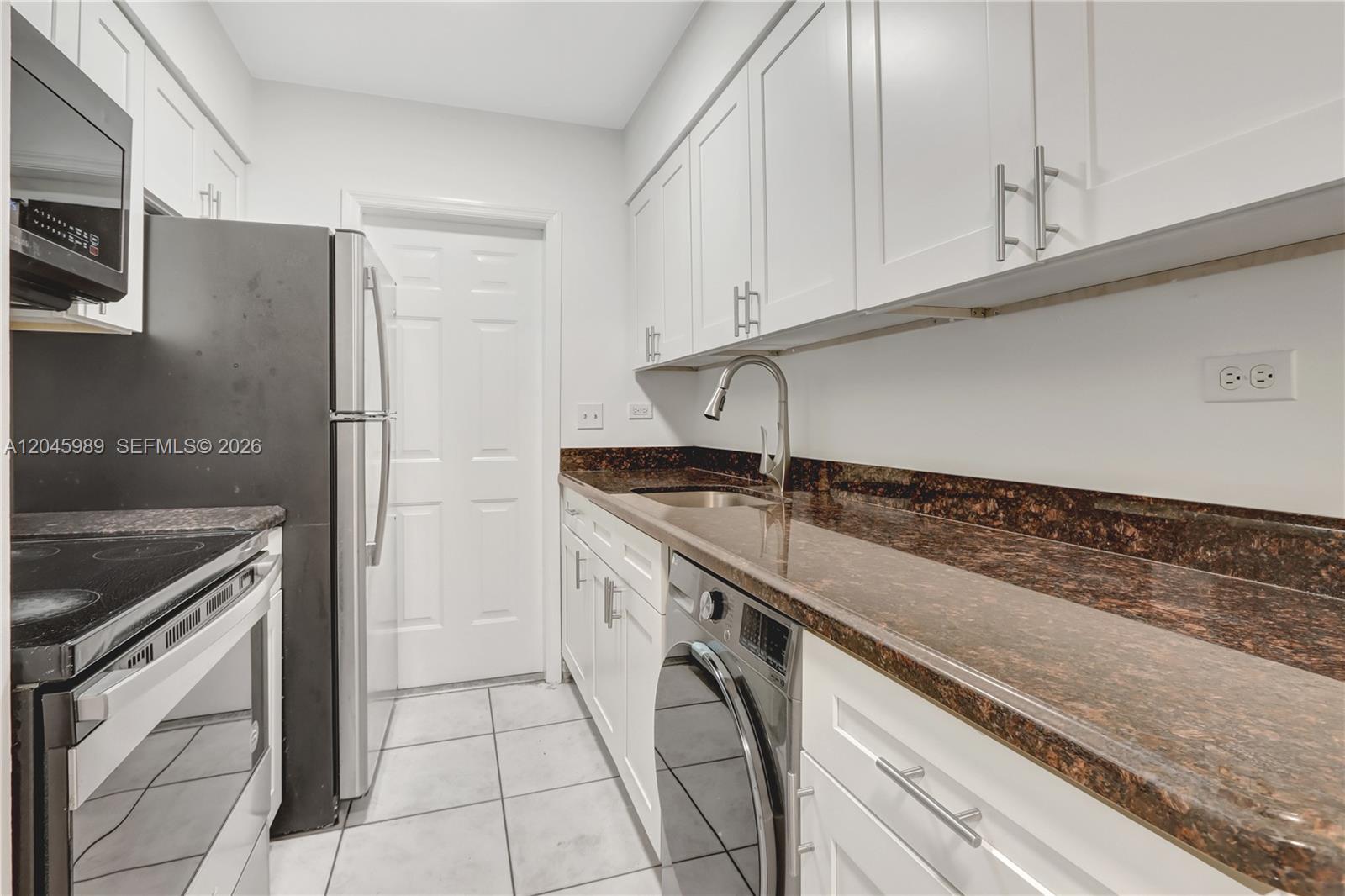 A galley kitchen features white cabinets, dark granite countertops, stainless steel appliances, and tile flooring — 202 N K St # 7, Lake Worth FL 33460, LAKE WORTH, FL