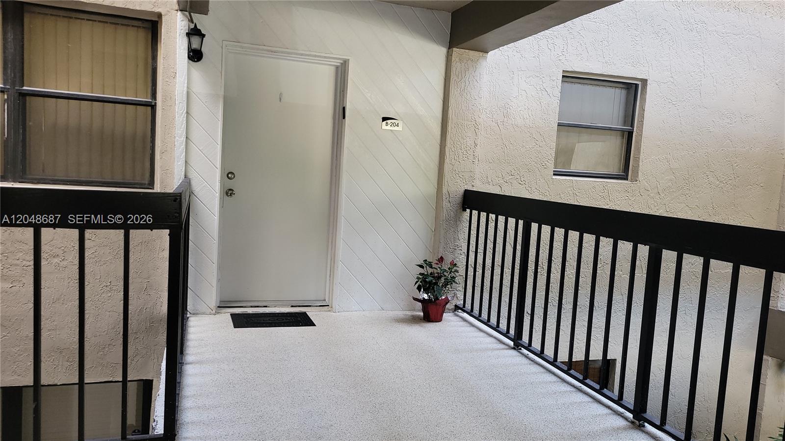 The exterior entryway of a residential unit features a white door, balcony railing, and plant — 461 Ives Dairy Rd # 2, Miami FL 33179, MIAMI, FL