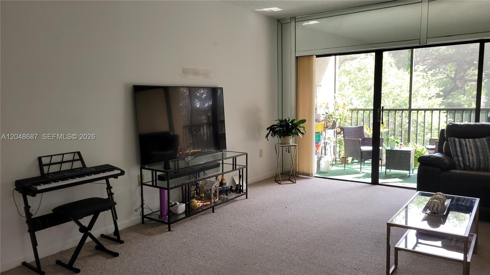 A living room features a television on a glass stand, a keyboard, and a balcony — 461 Ives Dairy Rd # 2, Miami FL 33179, MIAMI, FL