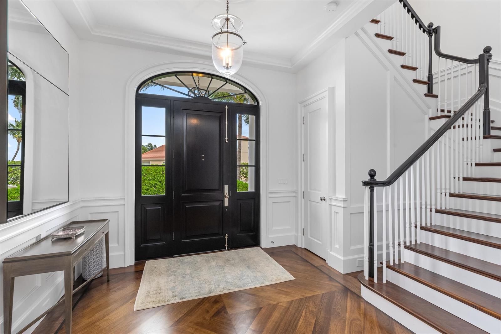 A bright foyer features a black front door, a wooden staircase, and herringbone hardwood floors — 102 Reef Road, Palm Beach FL 33480, PALM BEACH, FL