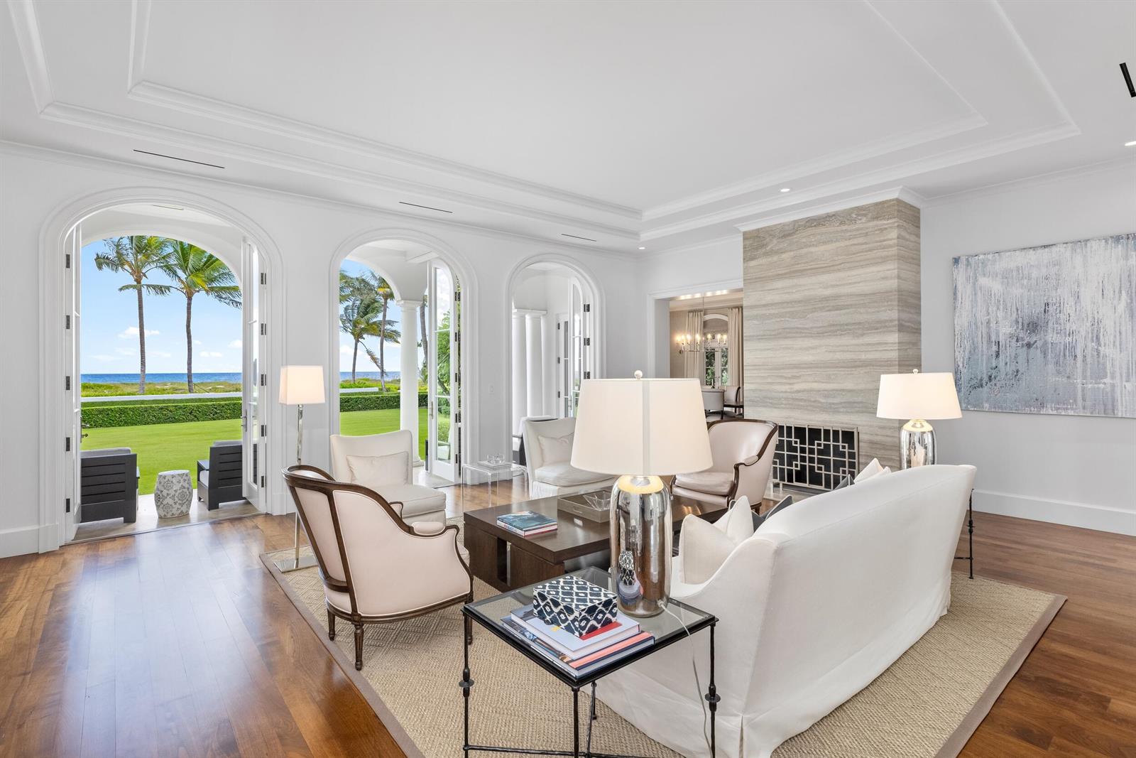 A bright living room features a stone fireplace, white furniture, and arched doors opening to oceanfront views — 102 Reef Road, Palm Beach FL 33480, PALM BEACH, FL