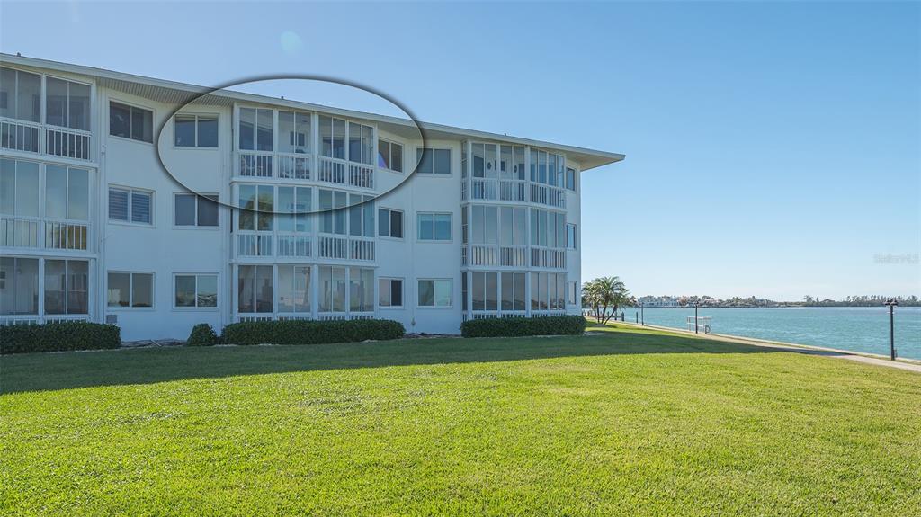 A multi-story apartment building with screened-in balconies overlooks a grassy lawn and the water — 777 JOHN RINGLING BOULEVARD UNIT 32, SARASOTA, FL