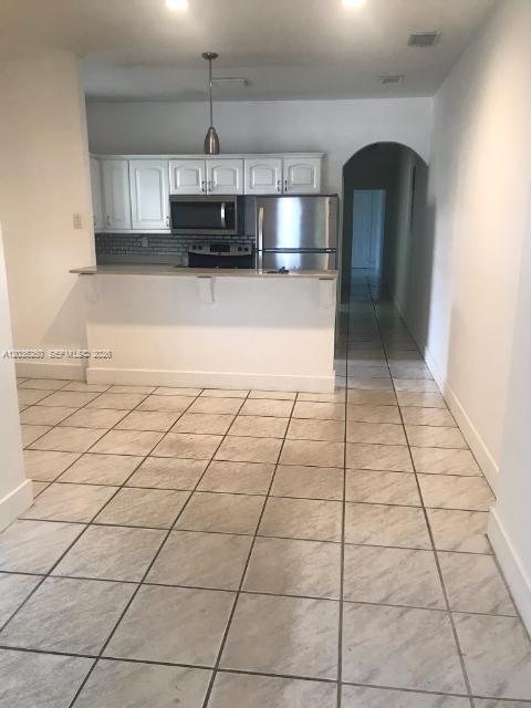 A kitchen features white cabinets, stainless steel appliances, and a breakfast bar over tiled floors — 3244 SW 3rd St # L, Miami FL 33135, MIAMI, FL