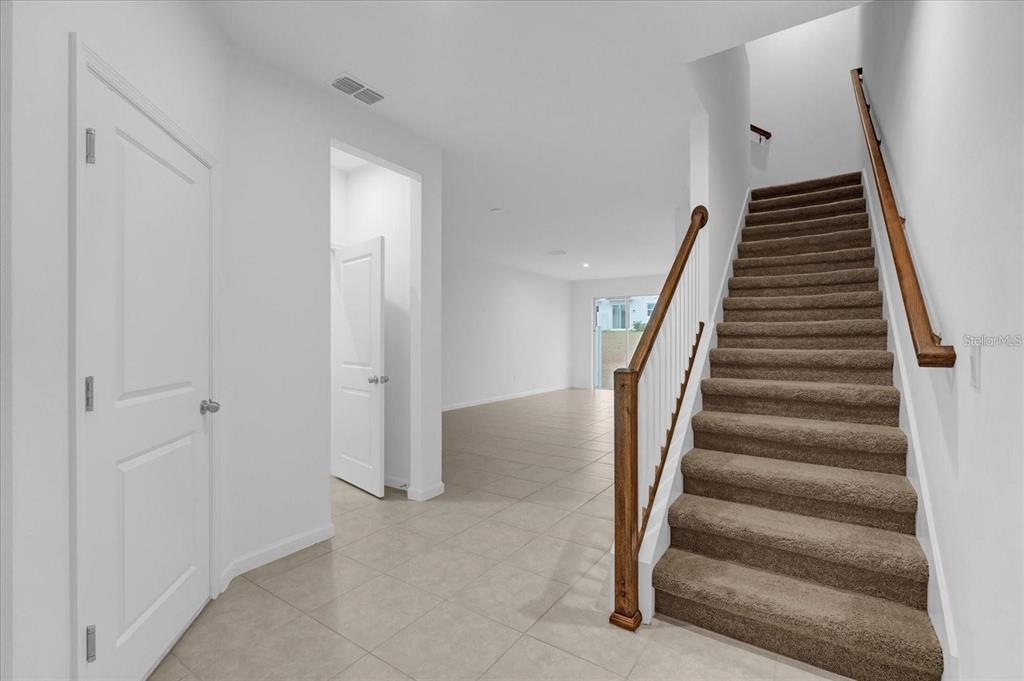 An entryway with tile flooring, a carpeted staircase with a wooden railing, and white walls — 1186 SEASIDE MIST TRAIL, KISSIMMEE, FL