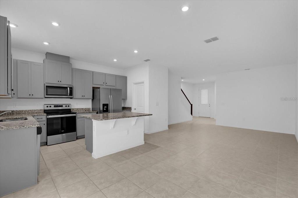 A kitchen with gray cabinets, granite countertops, and stainless steel appliances opens to a living area — 1186 SEASIDE MIST TRAIL, KISSIMMEE, FL