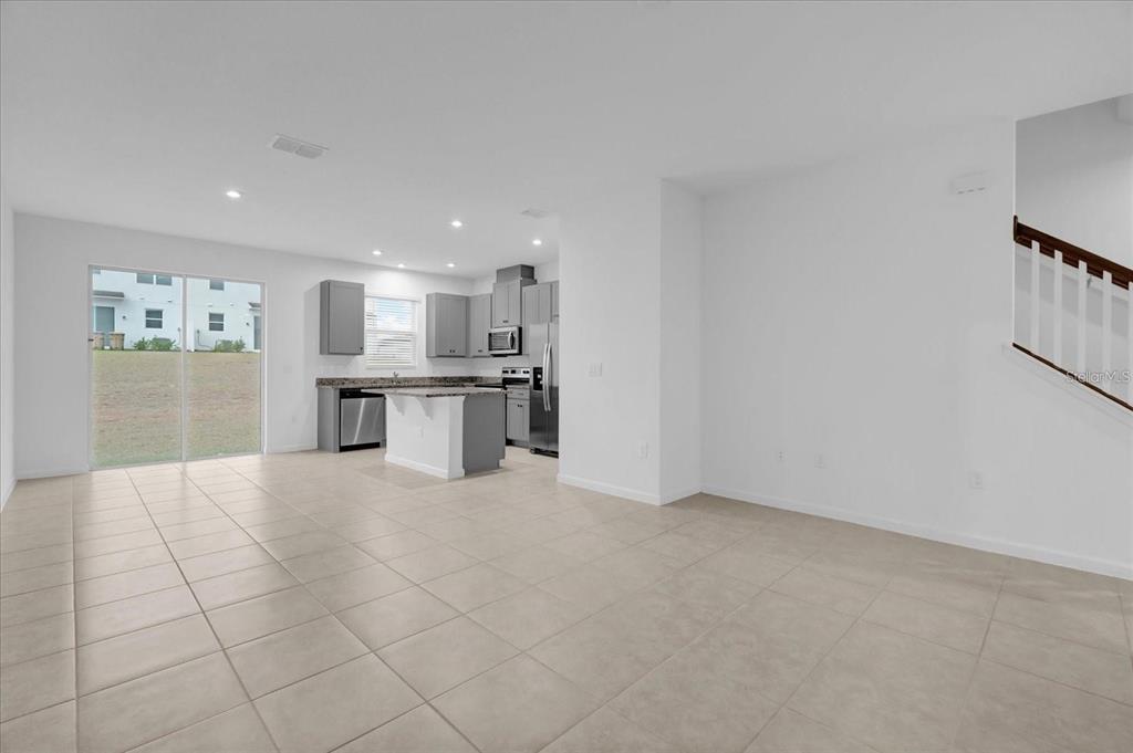 An open-concept kitchen and living area with tile flooring, gray cabinetry, and a sliding glass door — 1186 SEASIDE MIST TRAIL, KISSIMMEE, FL