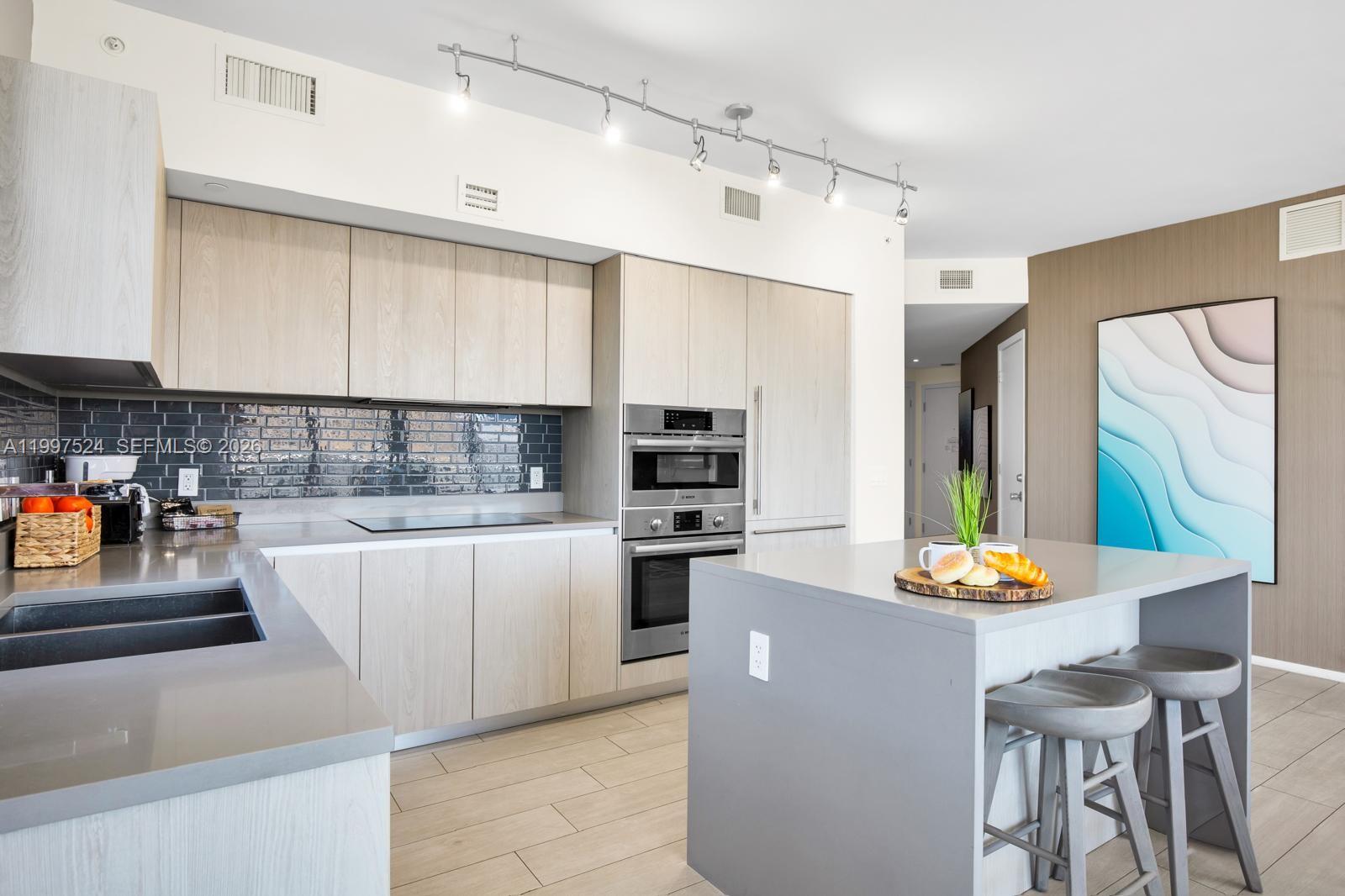 A modern kitchen features light wood cabinets, gray countertops, a central island, and stainless appliances — 4010 S Ocean Dr # R708, Hollywood FL 33019, HOLLYWOOD, FL