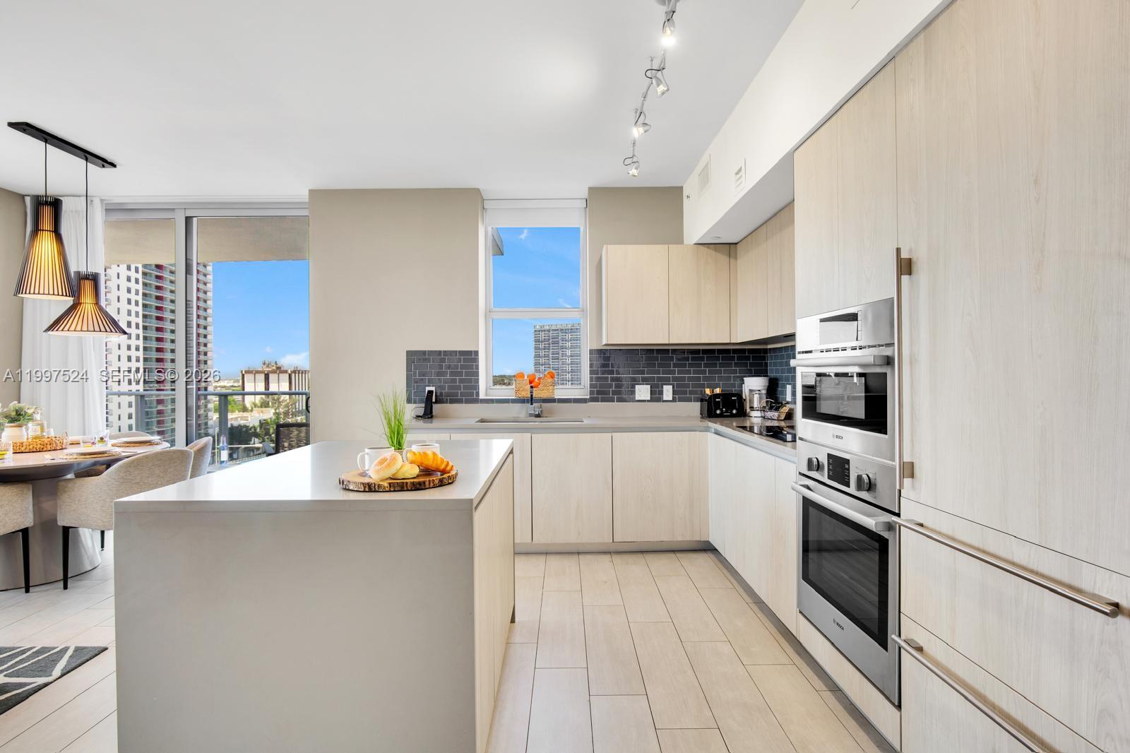 A modern kitchen features light wood cabinetry, stainless steel appliances, and a large central island — 4010 S Ocean Dr # R708, Hollywood FL 33019, HOLLYWOOD, FL