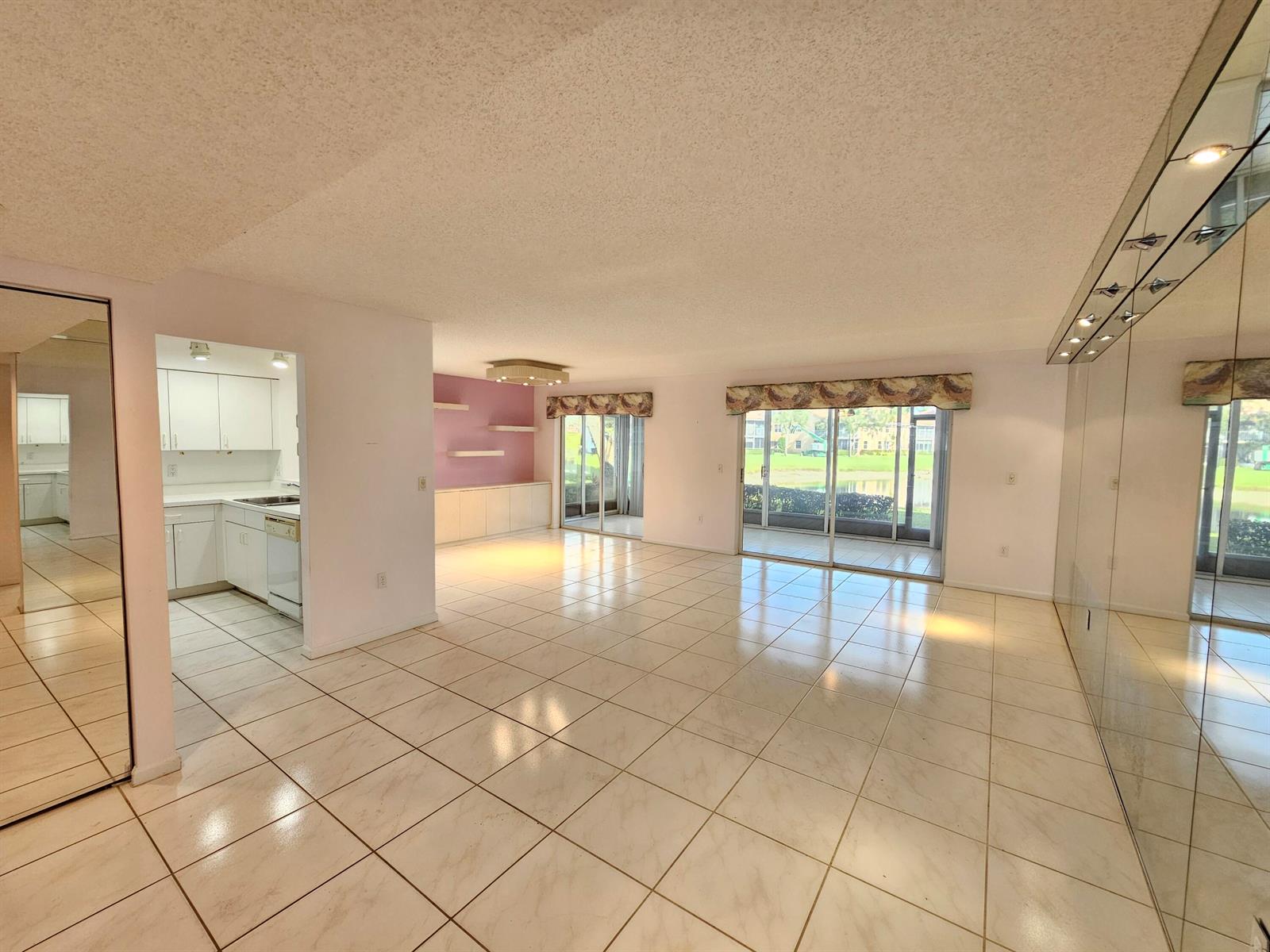 An open-concept living area with white tile floors, mirrored walls, and sliding glass patio doors — 9963 Seacrest Circle # 101, Boynton Beach FL 33437, BOYNTON BEACH, FL