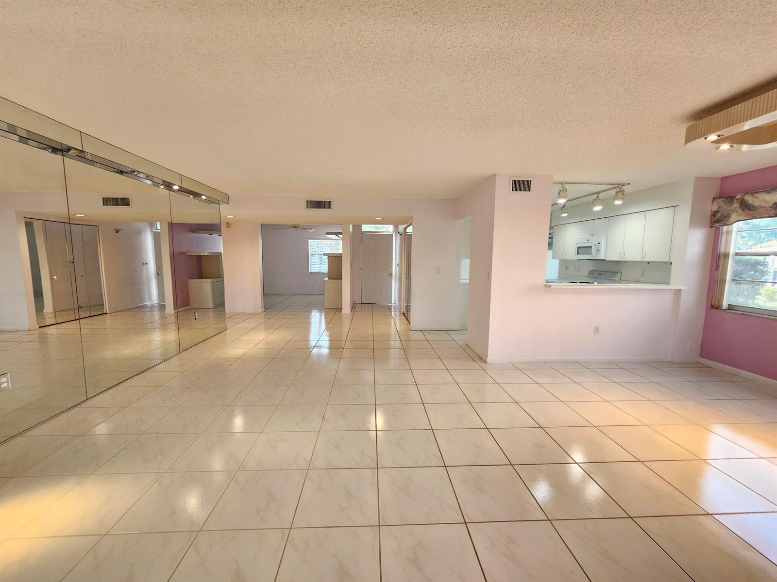 A spacious living area with white tile floors, mirrored walls, and an open kitchen pass-through — 9963 Seacrest Circle # 101, Boynton Beach FL 33437, BOYNTON BEACH, FL