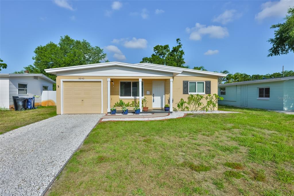 A single-story house with a tan exterior, a one-car garage, and a gravel driveway — 3242 KINGSTON STREET N, ST PETERSBURG, FL
