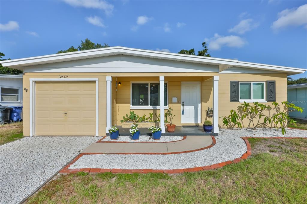 A yellow single-story house features a garage, a covered entryway, and a gravel front yard — 3242 KINGSTON STREET N, ST PETERSBURG, FL