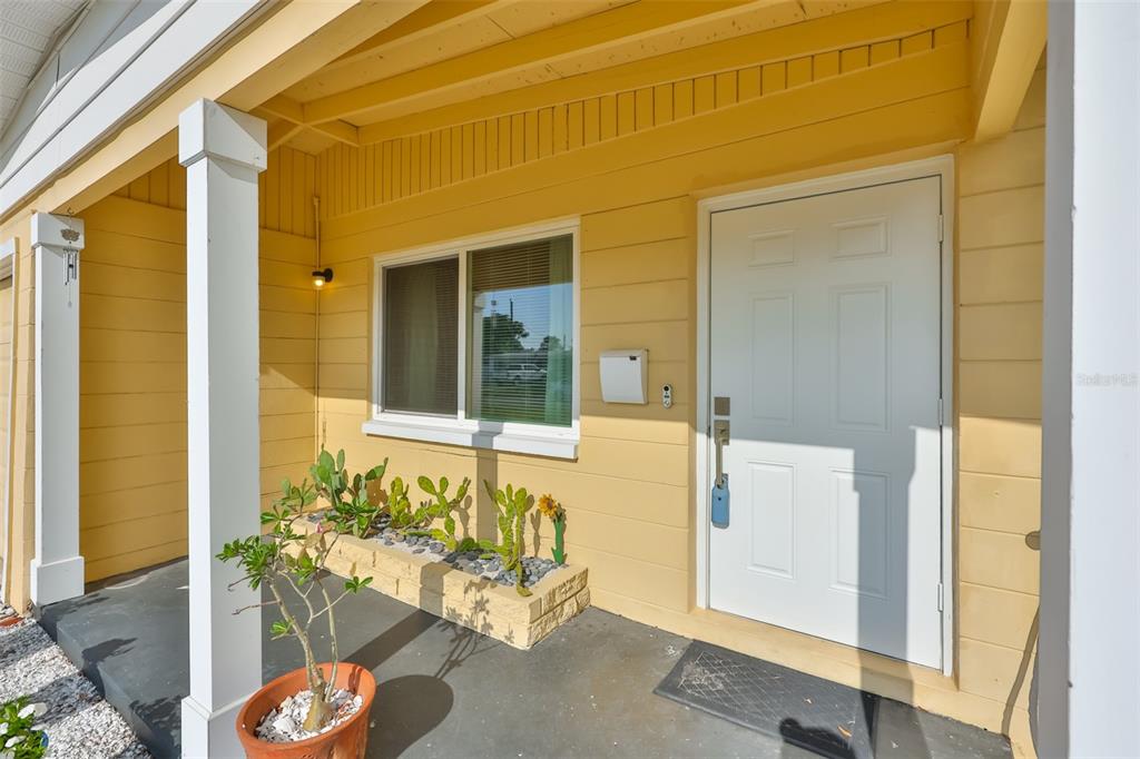 A yellow house exterior features a covered porch, a white front door, and a window — 3242 KINGSTON STREET N, ST PETERSBURG, FL