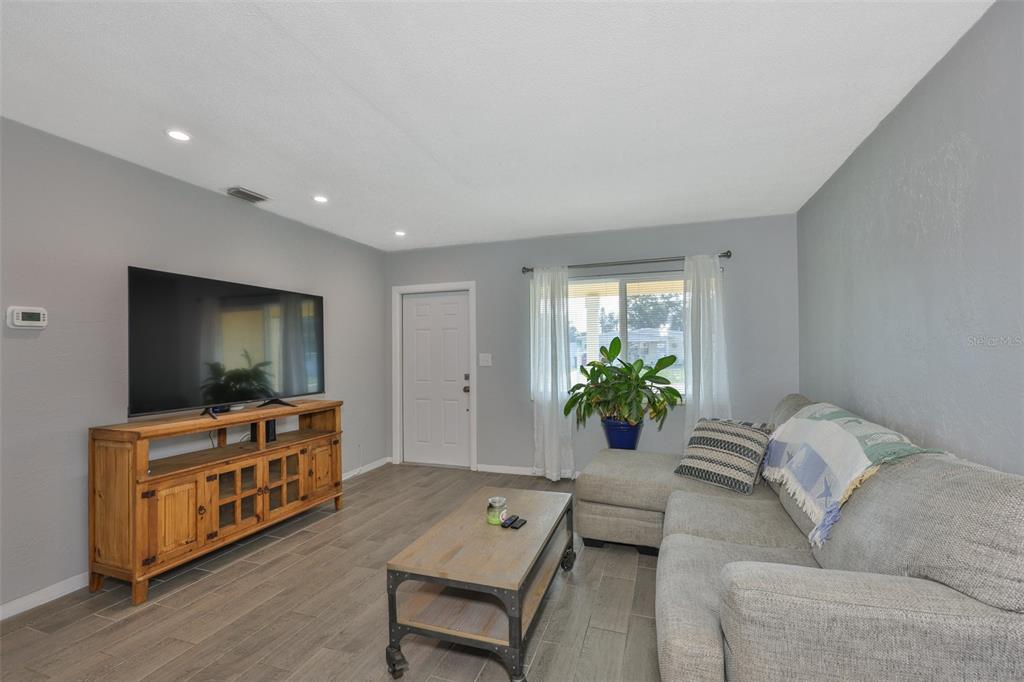 A living room features gray walls, wood-look tile flooring, a television console, and a sectional sofa — 3242 KINGSTON STREET N, ST PETERSBURG, FL
