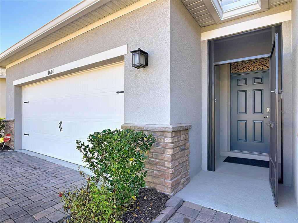 A view of a house exterior featuring a garage, stone accents, and an open front door — 1601 DELPHI WAY, NEW SMYRNA BEACH, FL