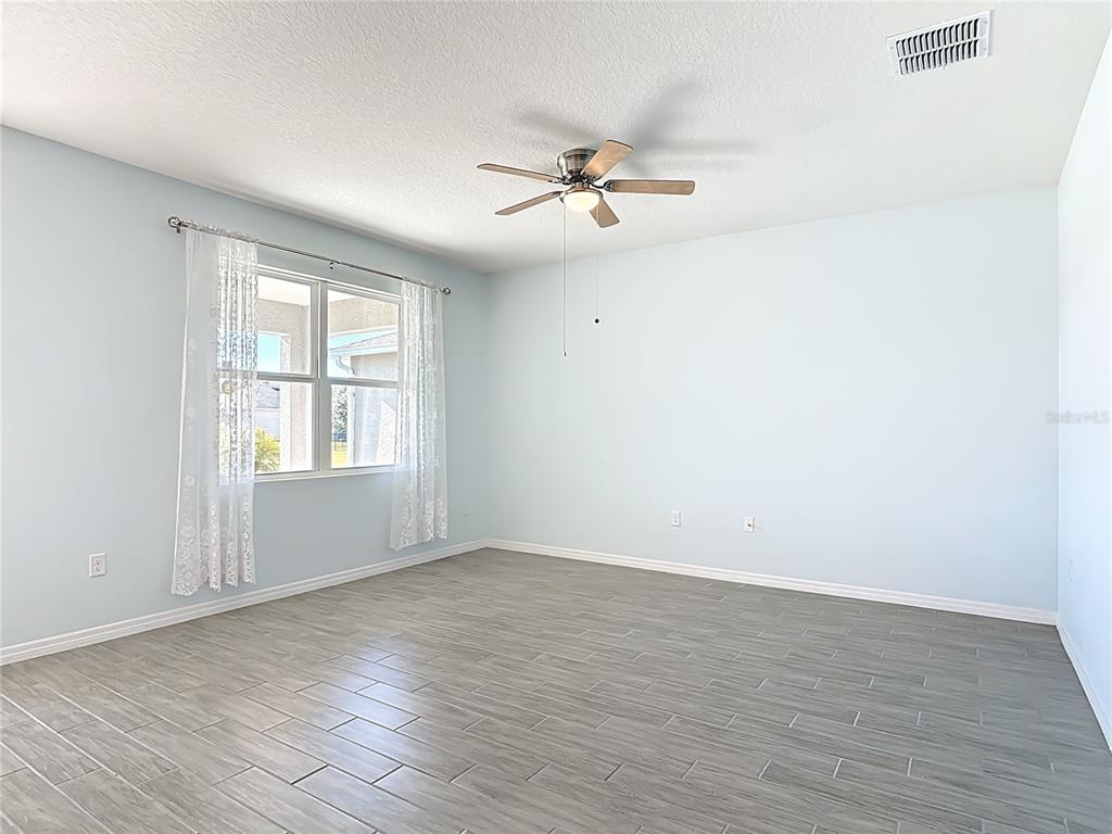 A bedroom with light blue walls, gray wood-look tile flooring, and a ceiling fan — 1601 DELPHI WAY, NEW SMYRNA BEACH, FL