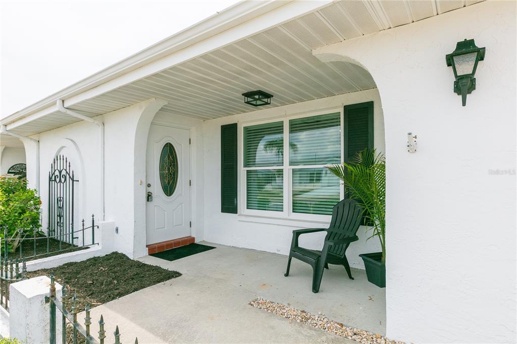 A white house exterior features a front porch with a black chair and door — 1616 BENTWOOD DRIVE, SUN CITY CENTER, FL