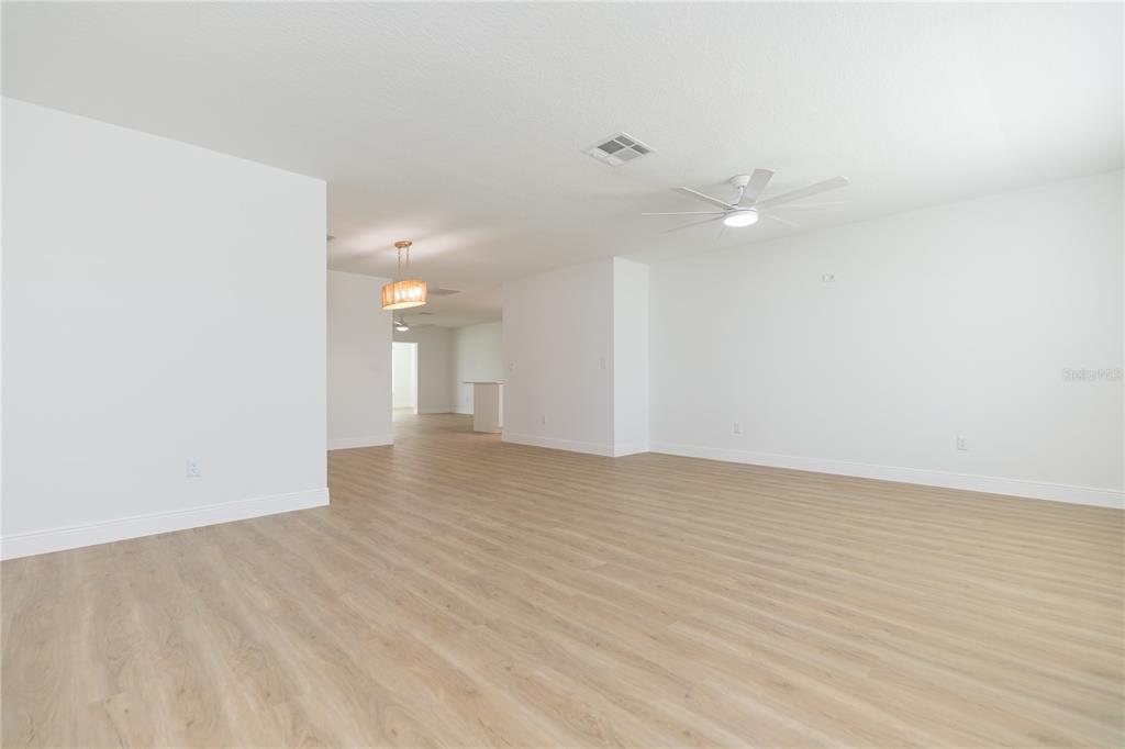 An open-concept living area features light wood-look flooring, white walls, and a ceiling fan — 1616 BENTWOOD DRIVE, SUN CITY CENTER, FL