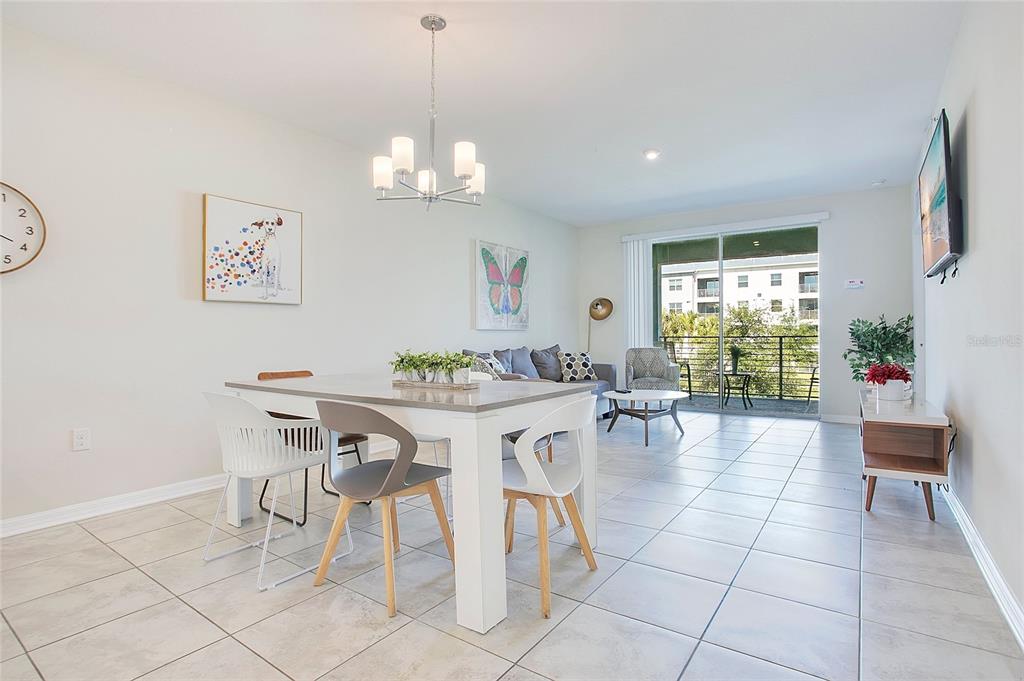 A bright open-concept dining and living area features tile flooring, a chandelier, and balcony access — 3120 PARADOX CIRCLE UNIT 204, KISSIMMEE, FL