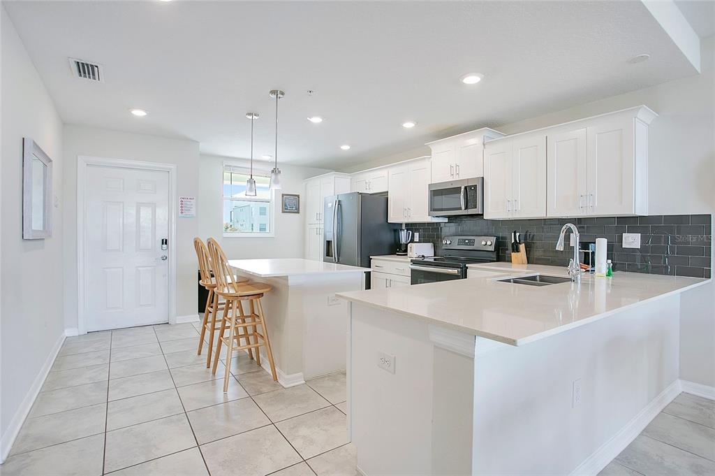 A modern kitchen features white cabinets, quartz countertops, a center island, and gray tile flooring — 3120 PARADOX CIRCLE UNIT 204, KISSIMMEE, FL