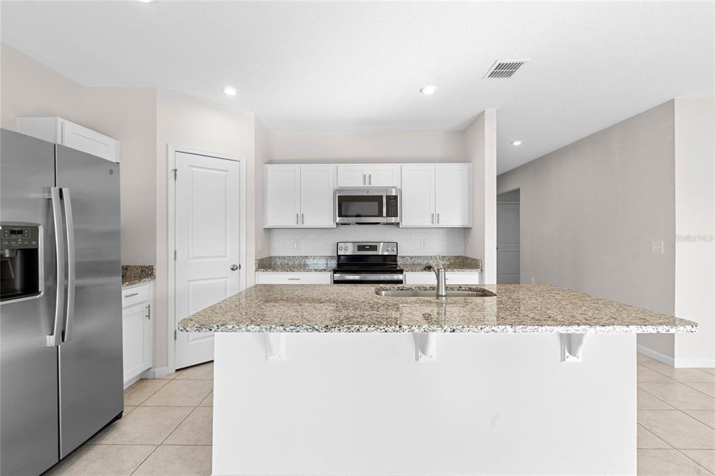 A kitchen features white cabinets, granite countertops, a stainless steel refrigerator, and a central island — 1125 CATSKILL DRIVE, HAINES CITY, FL