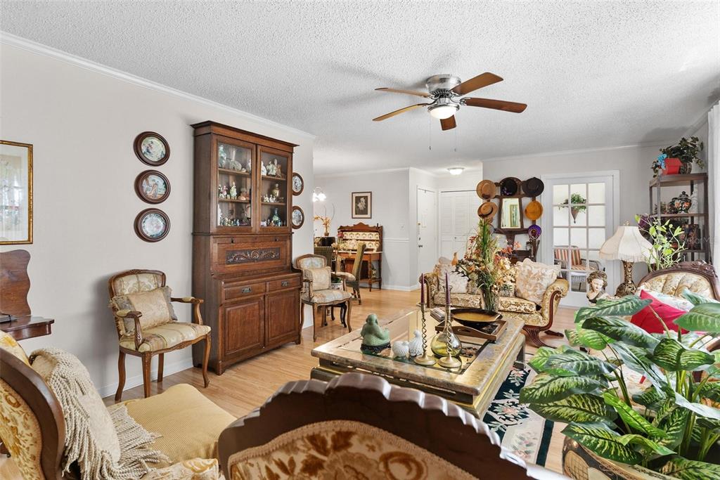 A living room features a wooden hutch, patterned armchairs, a glass coffee table, and a ceiling fan — 500 NEWELL HILL ROAD UNIT 108D, LEESBURG, FL