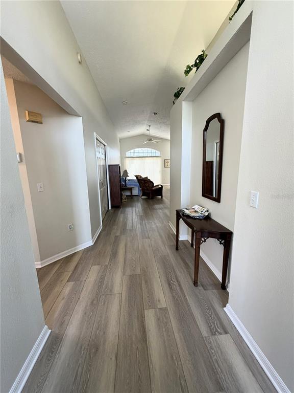 A hallway with wood-look flooring leads to a living area with a large window — 10542 MAGRATH LANE, NEW PORT RICHEY, FL