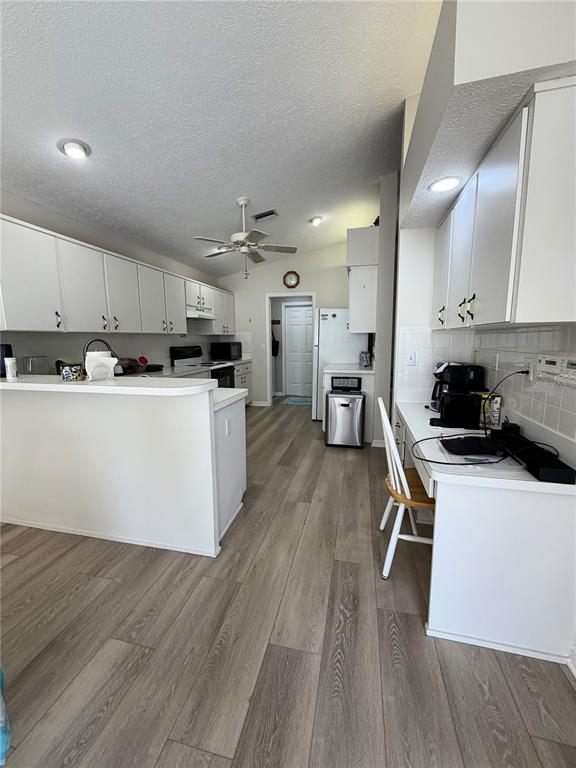 A kitchen features white cabinetry, a breakfast bar, and light wood-look flooring — 10542 MAGRATH LANE, NEW PORT RICHEY, FL