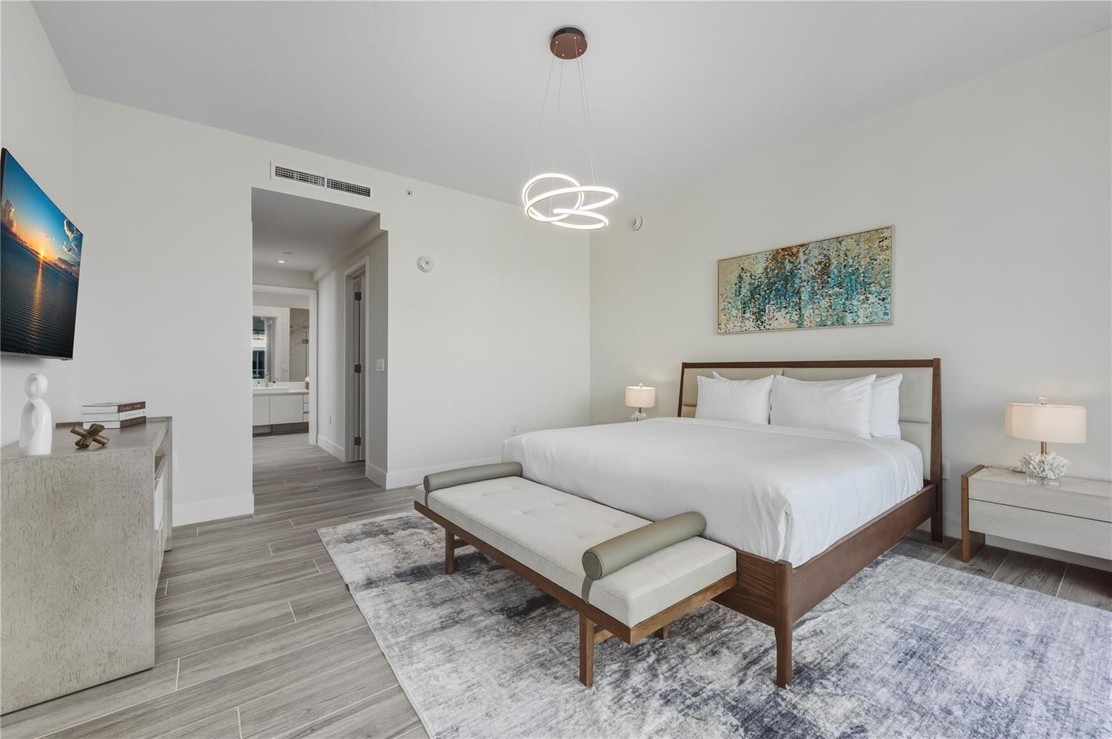 A modern bedroom features a king bed, a bench, a television, and a light fixture — 3100 N Ocean Drive, Riviera Beach FL 33404, RIVIERA BEACH, FL