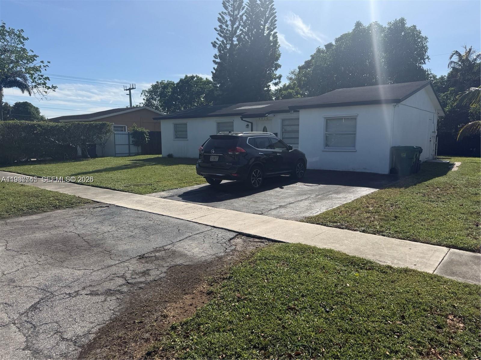 A white single-story house with a dark SUV parked in the driveway — 4910 NW 18th St, Lauderhill FL 33313, LAUDERHILL, FL