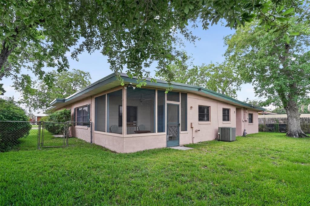A single-story house with a screened-in porch, pink exterior walls, and a large grassy yard — 580 GARDENIA CIRCLE, TITUSVILLE, FL