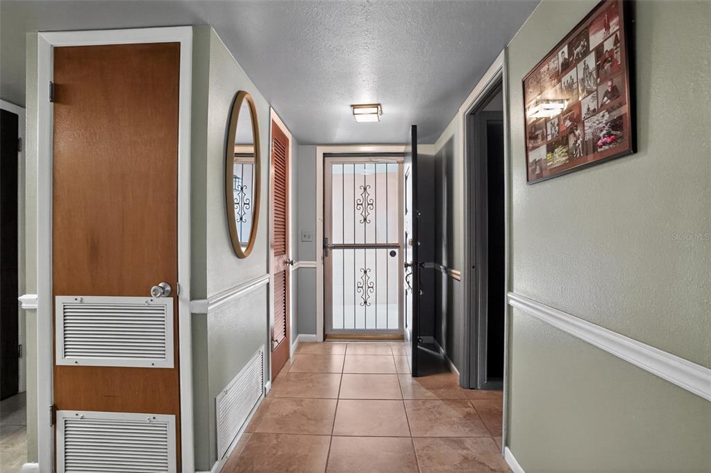 An entryway features tile flooring, a louvered closet door, a mirror, and a screen door — 580 GARDENIA CIRCLE, TITUSVILLE, FL