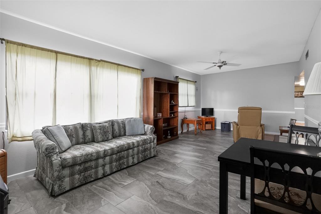 A living room with gray tile flooring, a patterned sofa, and a wooden bookshelf — 580 GARDENIA CIRCLE, TITUSVILLE, FL