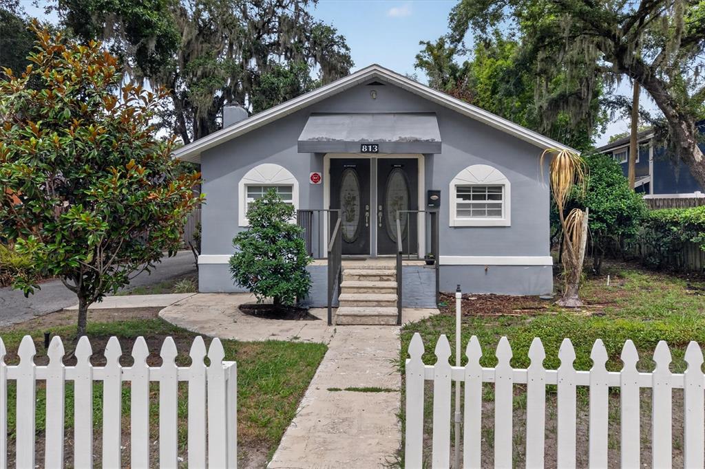 A gray, single-story house with a white picket fence and a central front entrance — 813 N FERN CREEK AVENUE, ORLANDO, FL