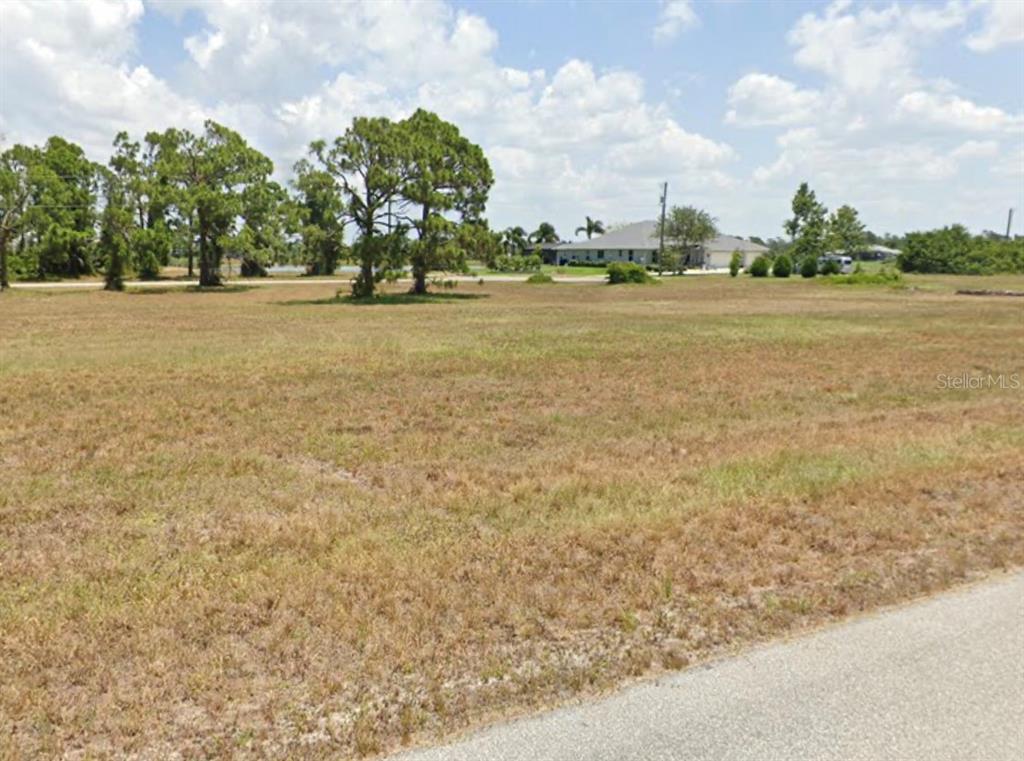 A large, flat, grassy vacant lot with scattered trees under a partly cloudy sky — 14 RUDDER LANE, PLACIDA, FL