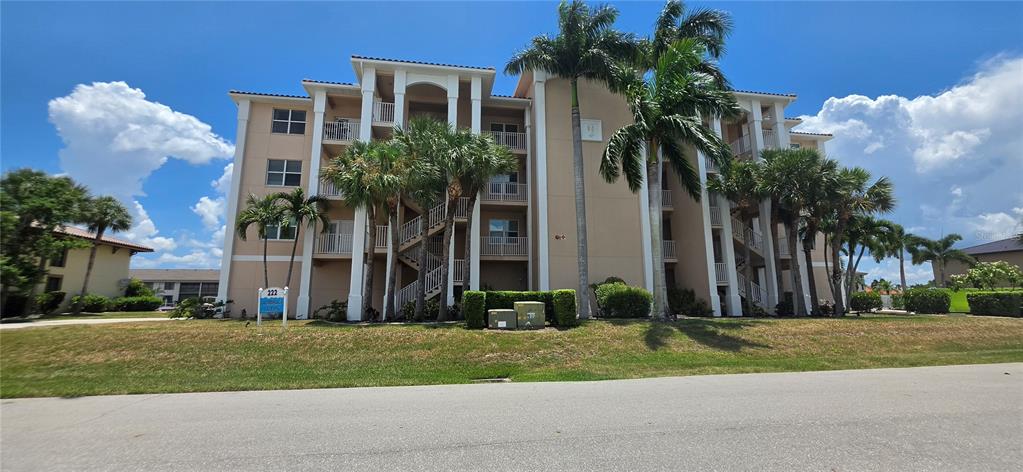 A multi-story beige apartment building features exterior staircases, balconies, and surrounding palm trees — 222 LEWIS CIRCLE UNIT 142, PUNTA GORDA, FL