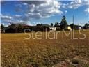 A vacant, grassy lot sits in front of several residential houses under a blue sky — 25450 ISLAS DRIVE, PUNTA GORDA, FL