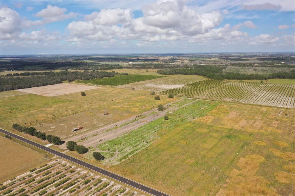 An aerial view shows a paved road bordering large, flat, open fields and agricultural land — LOT 11 LAKE BUFFUM ROAD S, FORT MEADE, FL