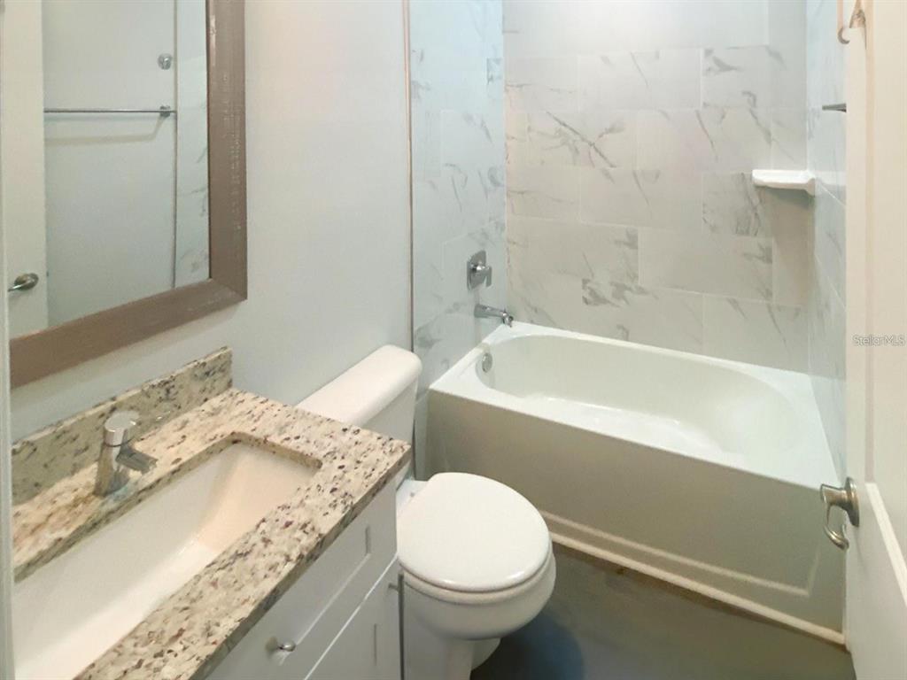 A bathroom features a granite vanity, a white toilet, and a tub with marble-look tiles — 13257 BLYTHEVILLE AVENUE, PORT CHARLOTTE, FL