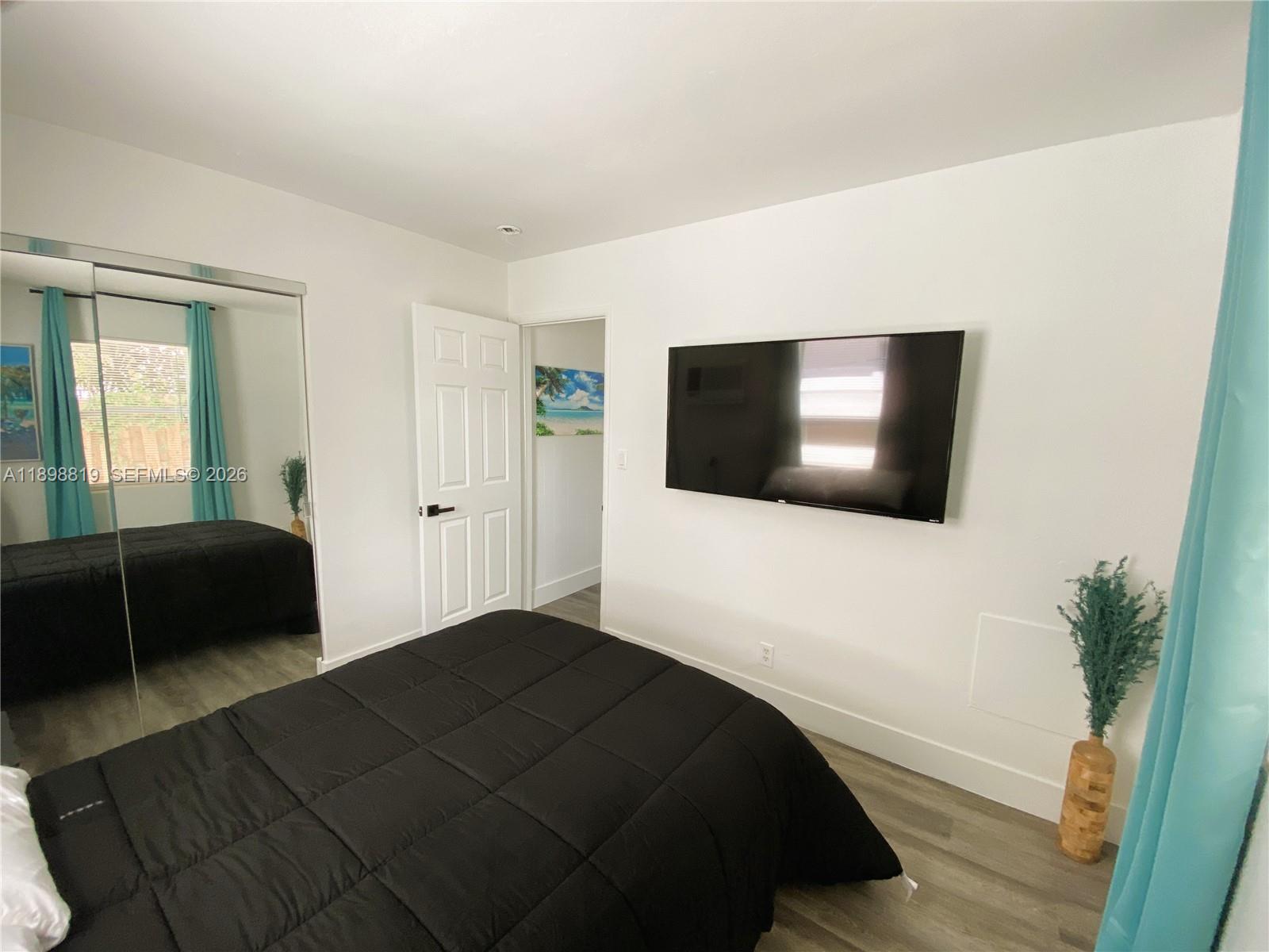 A bedroom features a black bed, a wall-mounted television, and mirrored closet doors — 3208 Canal Dr # 4, Pompano Beach FL 33062, POMPANO BEACH, FL