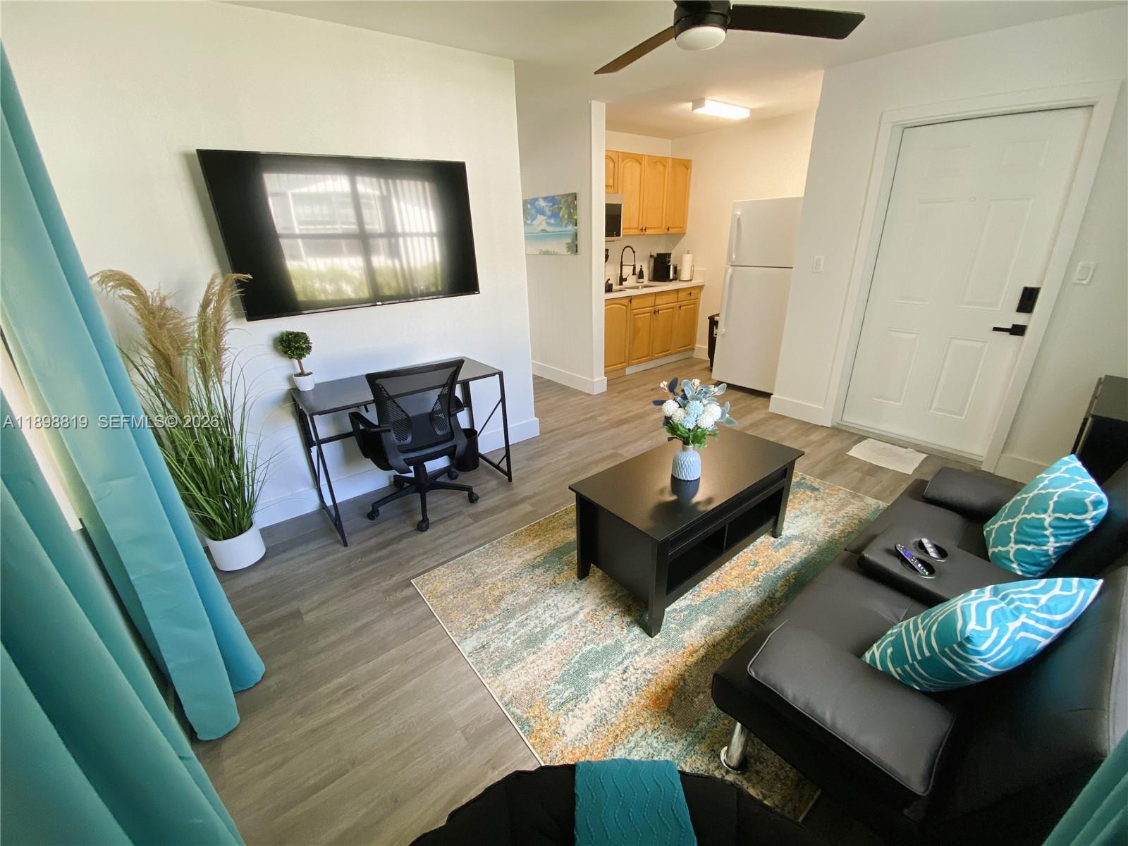 A living room features a black sofa, a desk, and an open kitchen with wood cabinets — 3208 Canal Dr # 4, Pompano Beach FL 33062, POMPANO BEACH, FL
