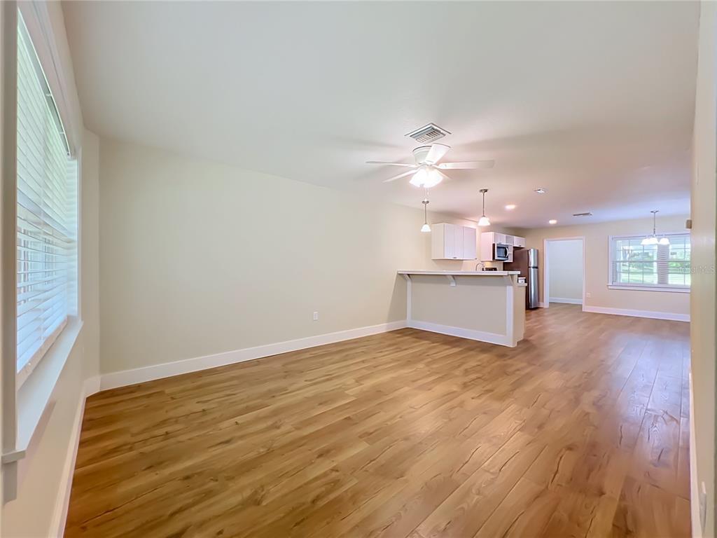 An open-concept living area with light wood-look flooring, a ceiling fan, and a kitchen peninsula — 450 LIBERTY AVENUE UNIT 3, MOUNT DORA, FL
