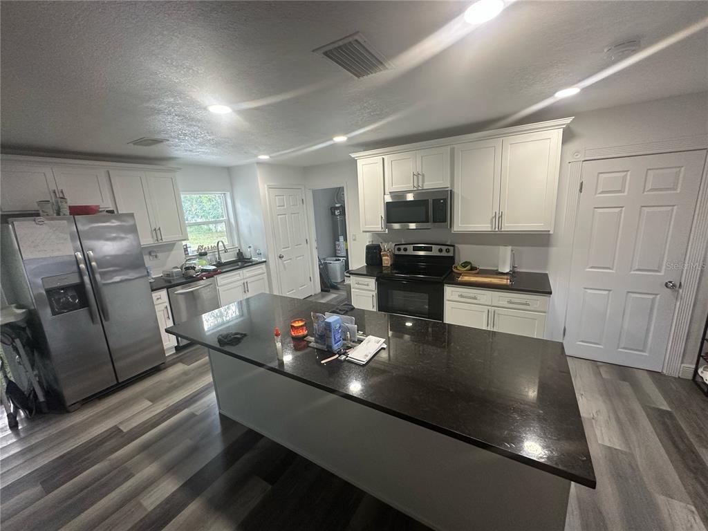 A kitchen features white cabinets, dark countertops, a central island, and stainless steel appliances — 1011 GERONA AVENUE, DELTONA, FL